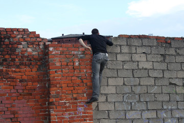 a man in dark clothes climbed onto an old brick fence and peeks over the wall