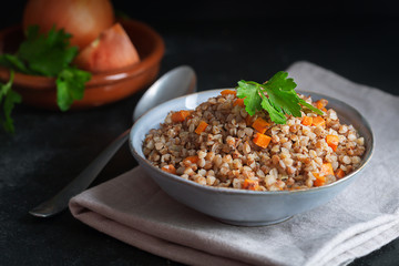 Boiled buckwheat cereal with carrot, parsley and butter in a bowl on a dark background. Traditional Russian dish on dark background