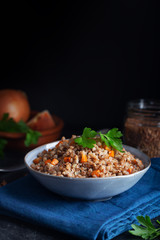 Boiled buckwheat cereal with carrot, parsley and butter in a bowl on a dark background. Traditional Russian dish on dark background with copy space