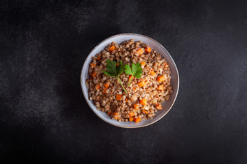 Boiled buckwheat cereal with carrot, parsley and butter in a bowl on a dark background. Traditional Russian dish on dark background