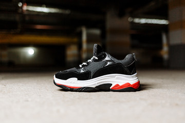 black sneaker on thick white with red accents soles on a gray concrete background