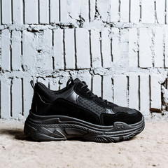black sneaker with thick soles on the cement floor against the background of brick wall