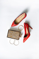 pair of red high-heeled shoes with pointed toes, decorated with metal blue inserts and metal clutch with sparcles on a white background