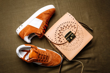brown suede sneakers with white accents on a white sole and a brown leather bag with a golden lock...