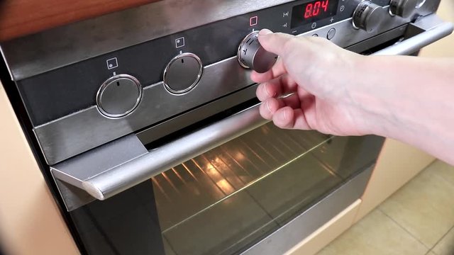 Woman turning, switching on the stove, baking oven and changing modes in order to preheat and cook meal