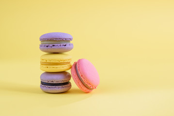 Tasty violet and yellow french macaron cakes on yellow background.