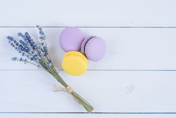 Delicious violet and yellow macarons and branch of fragrant lavender on white wooden background.