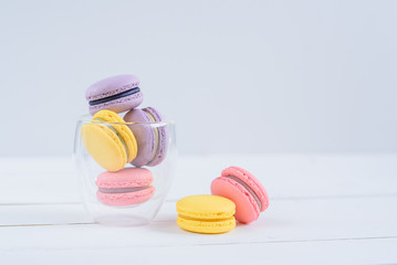Delicious colorful macarons in a transparent glass cup on white wooden background.