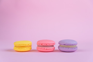 Tasty violet, pink and yellow french macaron cakes on pink background.