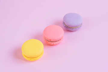 Tasty violet, pink and yellow french macaron cakes on pink background.
