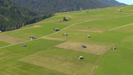Naklejka premium AERIAL: Flying above wooden shacks scattered around the vibrant green meadows.