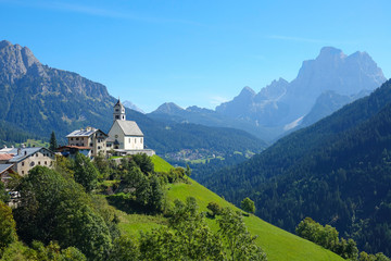 AERIAL: Small village on top of a green hill, surrounded by Italian Dolomites.
