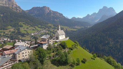 Fototapeta na wymiar DRONE: Flying over a church and a small graveyard on top of a hill in Dolomites.