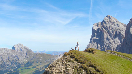 Obraz premium AERIAL: Woman observing the picturesque mountain landscape with her little dog.