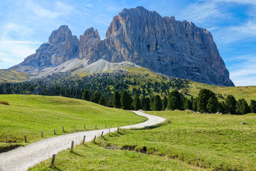 Fototapeta na wymiar Empty gravel road leads towards the majestic rocky mountain in the Dolomites.
