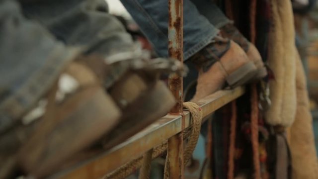 A hand held racking focus shot of a rope being untied off a metalllic bar where some people were seated with their cowboy shoes placed on it.