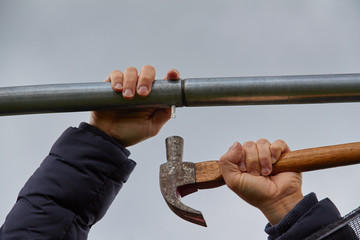 Using a hammer with women's hands to nail an aluminum bar. Grey sky background.