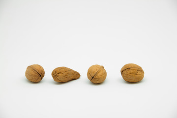 four walnuts in line on a white background in which one is a different walnut. Instead of being rounded it is elongated at the tip seeing its great difference.