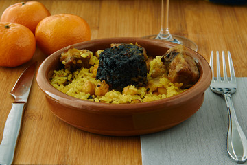 Baked rice in a pottery dish accompanied by pork, chickpeas, blood sausage, tomato and garlic....