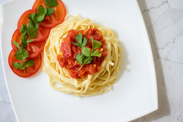 Pasta with fresh tomatoes, cooked with olive oil and garlic on a light background and a white square plate. Italian food. Horizontal orientation
