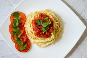 Pasta with fresh tomatoes, cooked with olive oil and garlic on a light background and a white square plate. Italian food. Horizontal orientation
