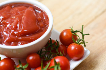 Ketchup in cup and fresh tomatoes on white plate
