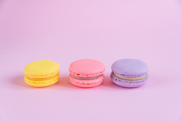 Tasty violet, pink and yellow french macaron cakes on pink background.