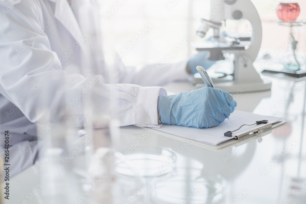 Wall mural a scientist hands writing on a clipboard in laboratory with test tube microscope and solutions.