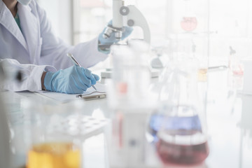 A scientist hands writing on a clipboard in laboratory with test tube microscope and solutions.