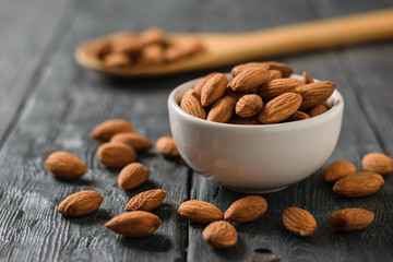 Almonds in a white bowl and a wooden spoon on a wooden table.