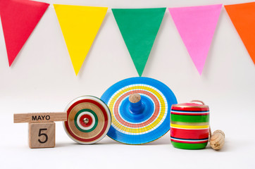 Wooden cube calendar with cinco de mayo date, yo-yo, spinning and balero, wooden mexican toys and colorful flags on white background