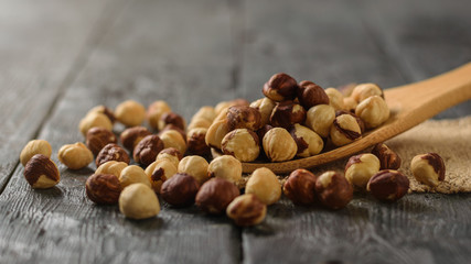 Roasted hazelnuts crumble from a spoon on a wooden table.