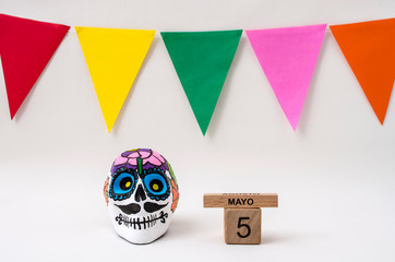 Hand painted styrofoam skull, wooden calendar with the date 5 de mayo and colorful paper  flags on...