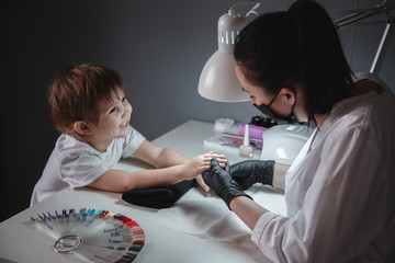 A little girl in a beauty salon. Looks at the manicurist in a black mask and black gloves. Nail...