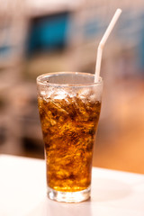 A glass of cola with ice on white table