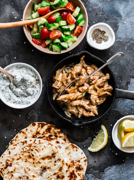 Ingredients for greek chicken gyros - fried chicken, tomato cucumber salad, tzatziki sauce and flatbread on a dark background, top view. Flat lay