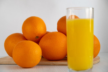 A glass of orange juice is on the table next to oranges.