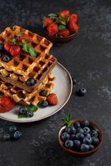 Chocolate and vanilla Belgian waffles with fresh berries on a ceramic plate on brown background. Sweet breakfast