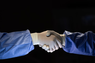 Two doctors in surgery cloth with rubber gloves shaking hands with team confident before start to do cure operation in dark surgery room - 265419441