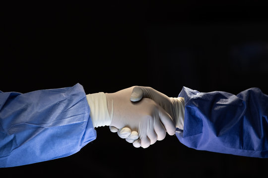 Two Doctors In Surgery Cloth With Rubber Gloves Shaking Hands With Team Confident Before Start To Do Cure Operation In Dark Surgery Room