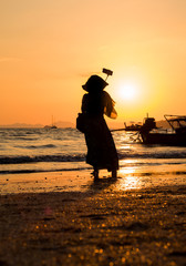 Asian woman taking selfies at the beach at sunset i