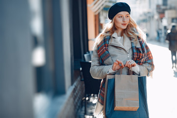 Elegant lady in a winter city. Stylish girl walking with shopping bags. Blonde in a cute beret