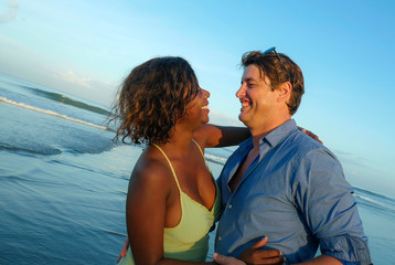  happy and romantic mixed race couple with attractive black African American woman and Caucasian man playing on beach having fun enjoying holidays in multiracial love