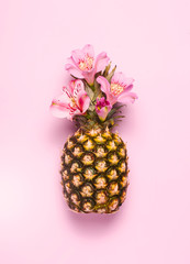 Pineapple with exotic flowers on pink background. Top view, flat lay.
