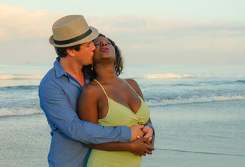 happy and beautiful mixed ethnicity couple with beautiful afro American woman and cheerful Caucasian man enjoying holidays honeymoon trip on beach cuddling sweet
