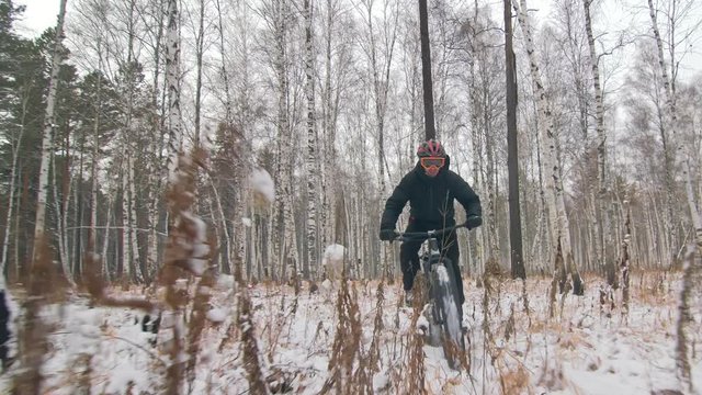 Professional extreme sportsman biker riding a fat bike in outdoors. Cyclist ride in winter snow forest. Man does trick on mountain bicycle with big tire in helmet and glasses. Slow motion in 60fps.