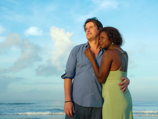 happy and beautiful mixed ethnicity couple with beautiful afro American woman and cheerful Caucasian man enjoying holidays honeymoon trip on beach cuddling sweet