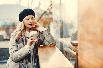 Elegant lady in a winter city. Stylish girl drinking a coffee.  Blonde in a cute beret