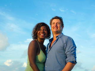 happy and beautiful mixed ethnicity couple with beautiful afro American woman and cheerful Caucasian man enjoying holidays honeymoon trip on beach cuddling