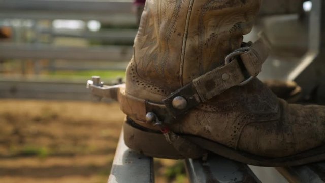 A still close up of a person wearing a cowboy's boot as the boot is placed on a metal stand on a warm and sunny day.